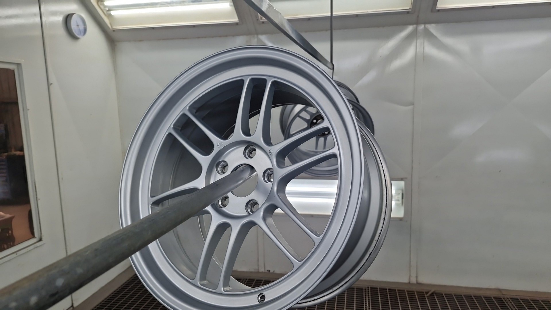 Silver alloy wheel suspended in the spray booth for refinishing